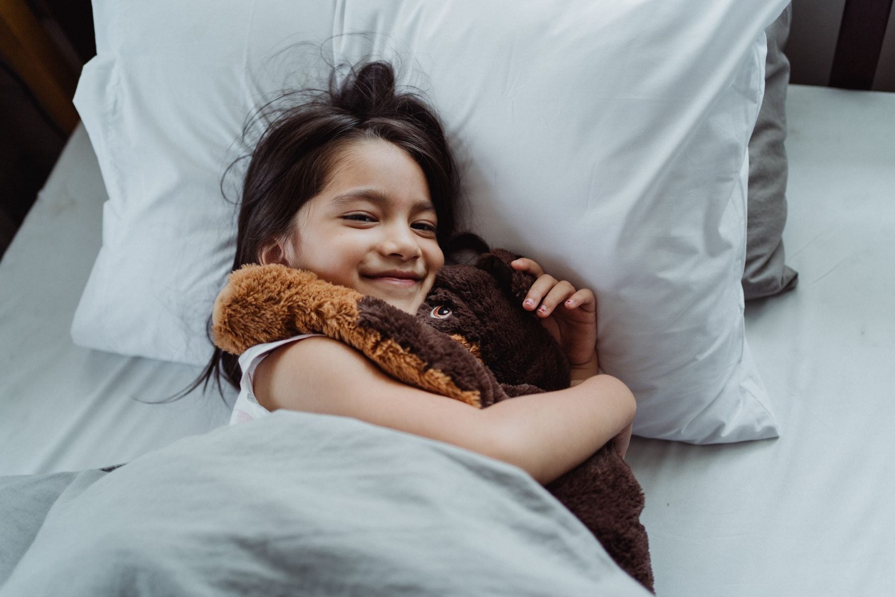 Une fillette sourit dans son lit, son doudou contre elle