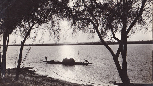 Pirogue chargée sur un grand fleuve bordé d’arbres, photographie ancienne en sépia, article sur Pierre Mille