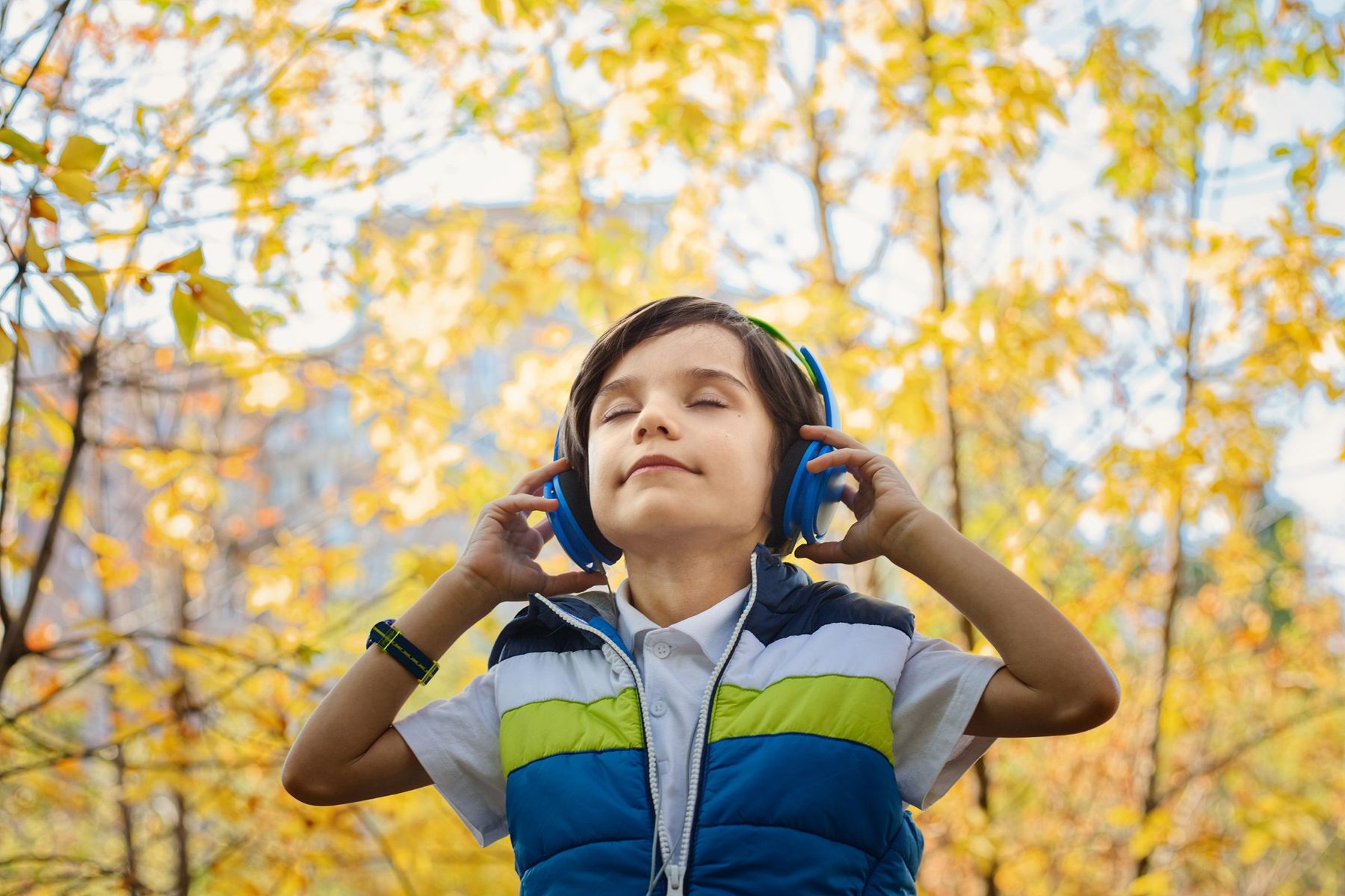 Un garçon écoute, les yeux fermés, un casque sur les oreilles, dans un parc en automne